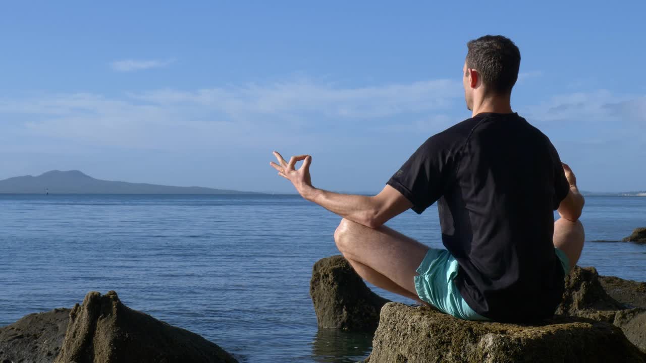 아침에 해변에서 바위에 요가 포즈에서 명상하는 젊은 맞는 남자