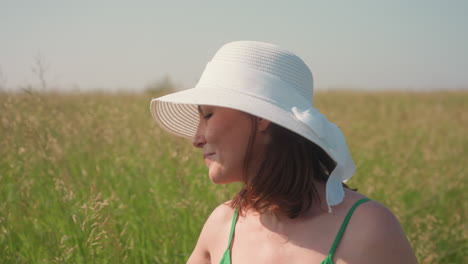 young woman wearing green dress and white sunhat walking through tall barley field gently touching stalks under warm sunlight, embraced by serene summer countryside