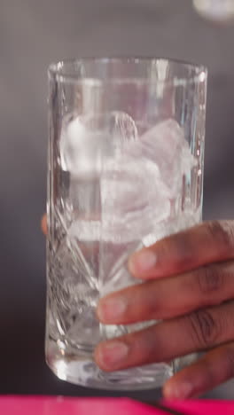 el camarero vierte hielo en un vaso de cristal usando una cuchara de primer plano. el camarero afroamericano prepara cócteles para los invitados en el bar. cubos de hielo para bebidas frescas