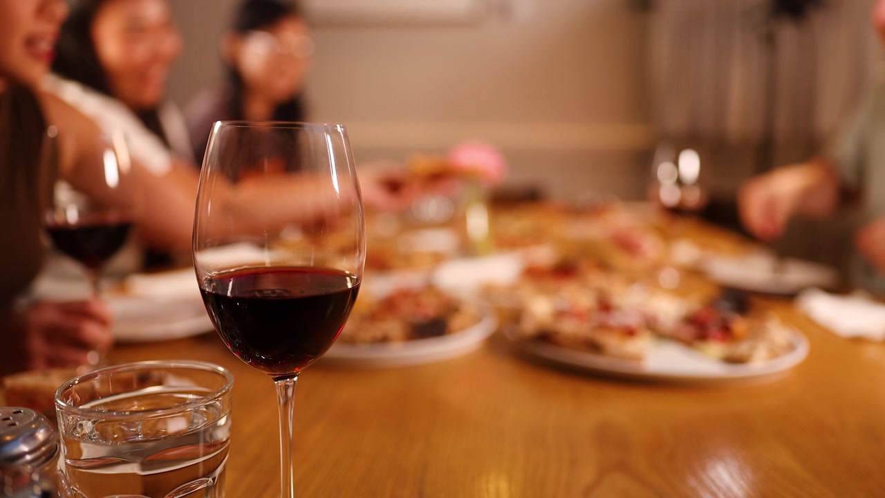 Amici di diverse etnie gustano pizza e vino rosso durante una cena sociale in un'illuminazione calda del ristorante.