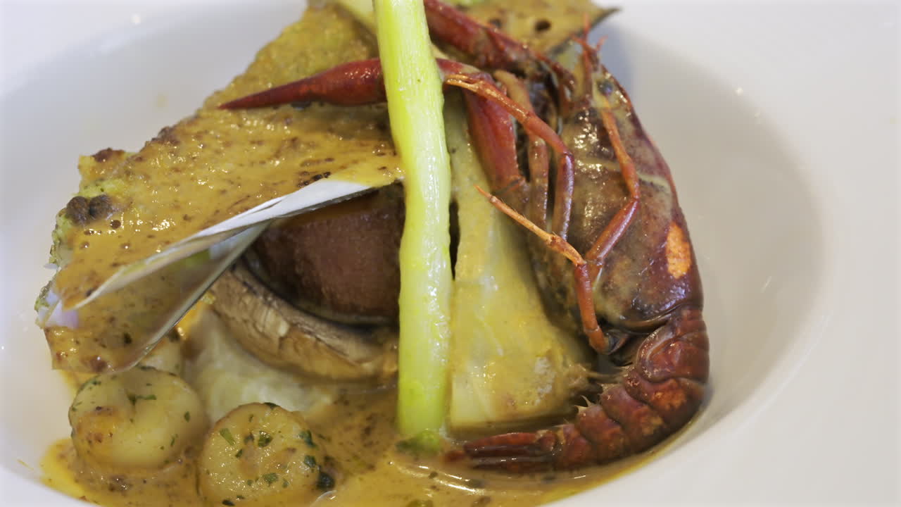 Close up of whole cooked crayfish with a mussel shell filled and a creamy herb topping on a white plate
