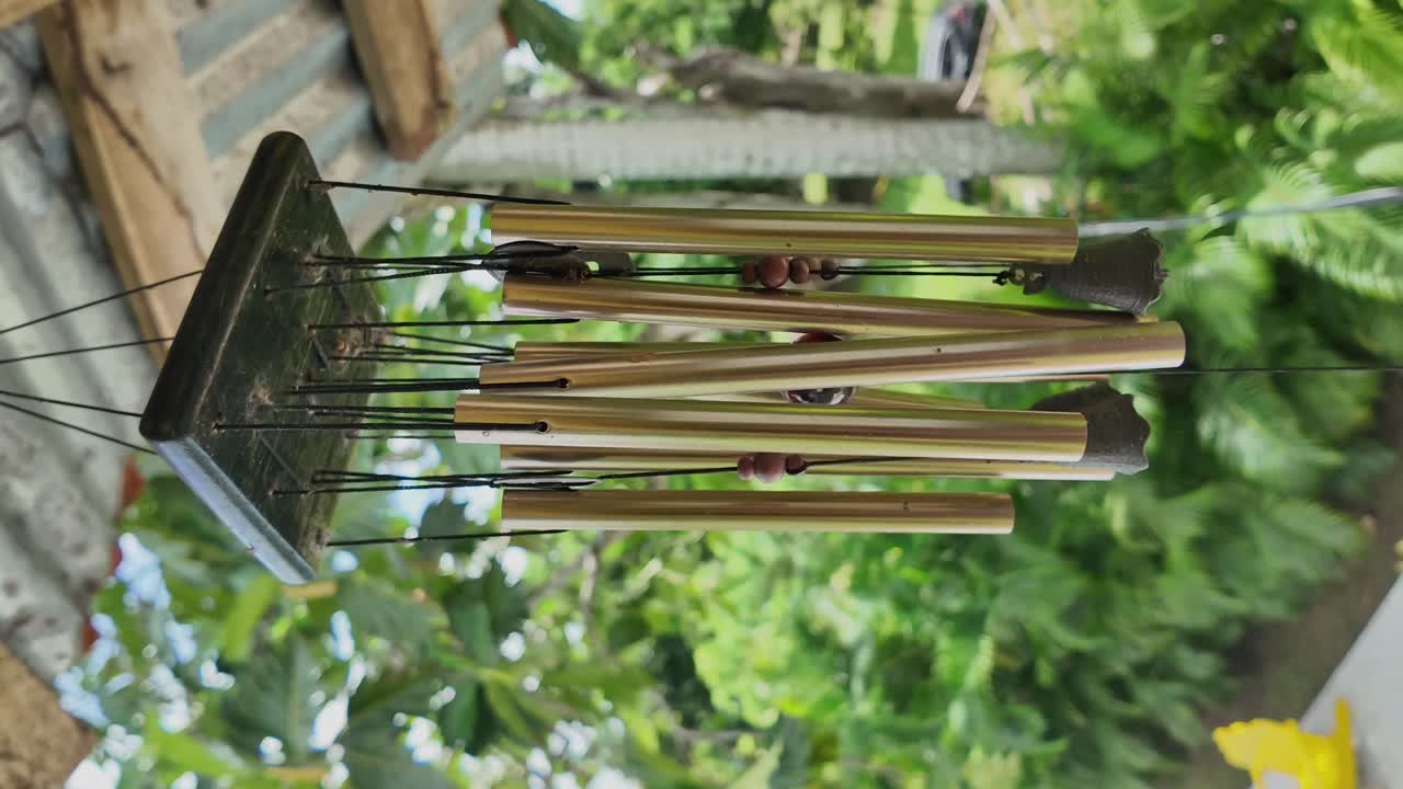 Vertical shot of golden wind chime with wooden base gently swaying in the breeze, creating a soothing sound