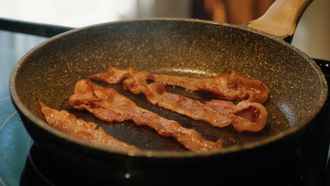 close up of bacon slices slowly cooking in a pan at slow motion