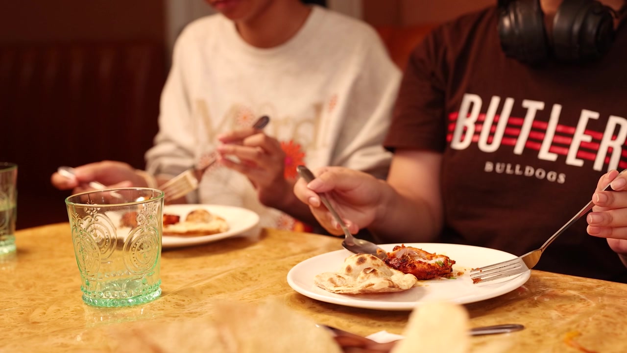 Close-up shot of diners using forks to eat Indian cuisine in a warm restaurant setting.