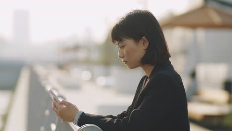 asian businesswoman using mobile phone on urban embankment