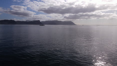 Drone-shot-over-still-ocean-water-along-the-shoreline-towards-a-mountain-range