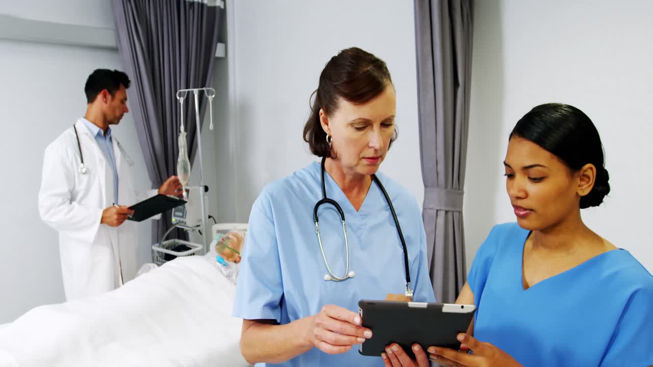 enfermeras discutiendo sobre una tableta digital mientras el médico revisa un goteo intravenoso en el paciente