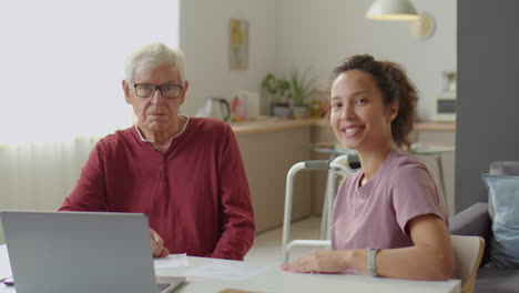 portrait of caregiver and senior man at desk with laptop