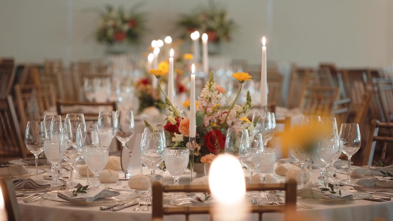 Elegant borddækning til et bryllup eller en gallafest med hvide dug, krystalglas, blomsterdekorationer og tændte stearinlys