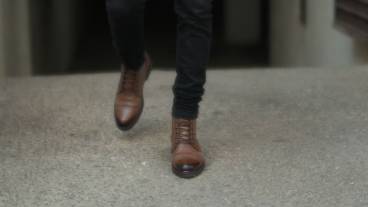 Feet Of A Male Model In Brown Leather Boots Walking On The Floor. cropped shot