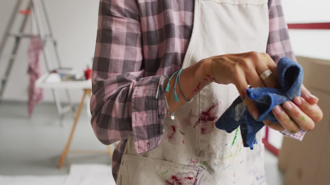 Video of midsection of biracial female artist cleaning hands with cloth