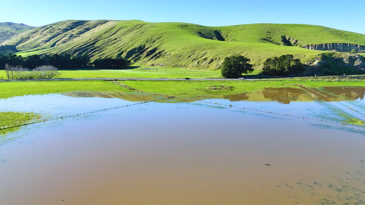 Aerial view of Akaroa&#x27;s vibrant green hills and reflective water under bright sunlight, showcasing natural beauty and tranquility