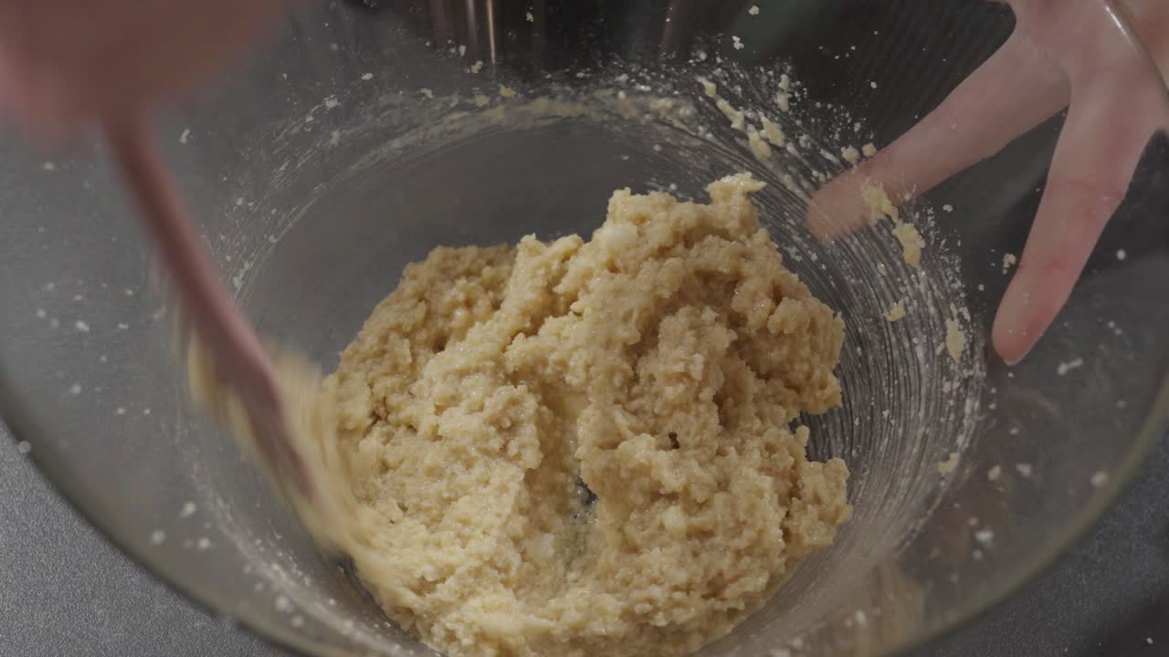 Primo piano al rallentatore: mescolare l'impasto dei biscotti con un cucchiaio di legno in una ciotola di vetro.