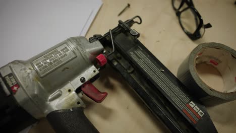 nail gun, nails, tape and glasses from above on wood work bench