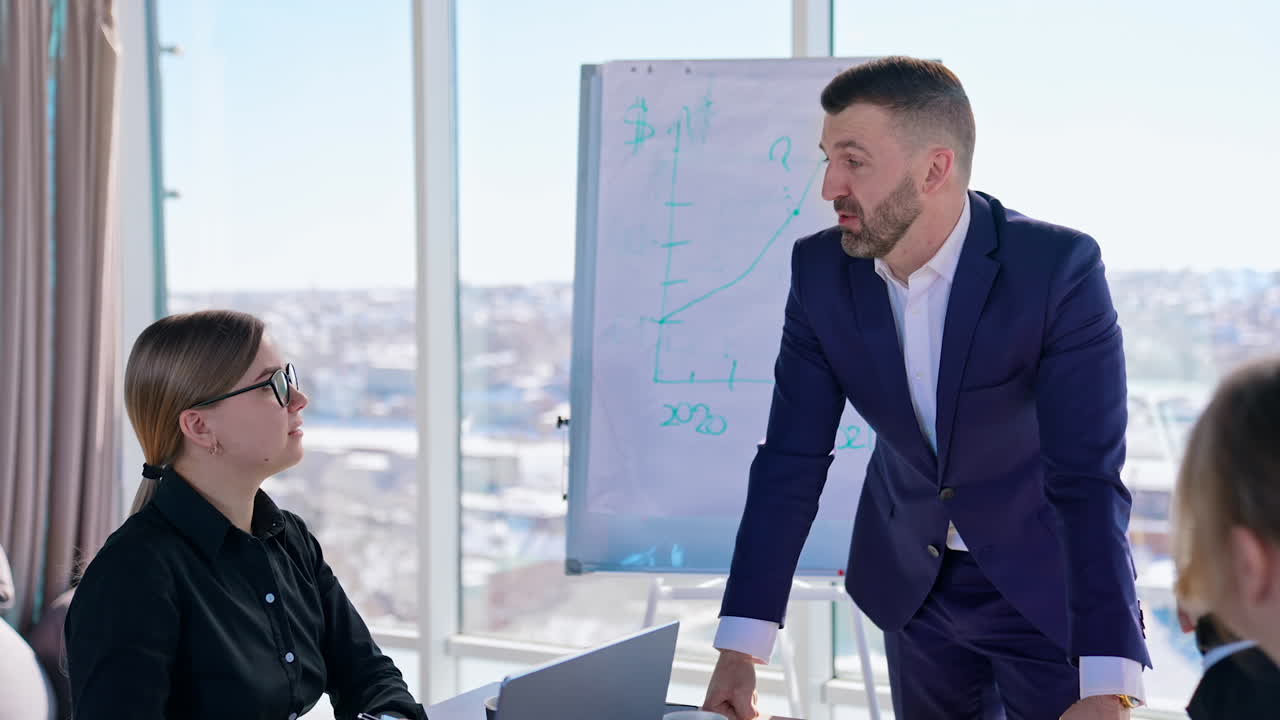 Business conversation in office. Business colleagues sit at table and listen to entrepreneur in elegant suit on the large window background with a city view.
