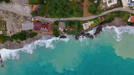 drone top down tracking pan above coastal highway and homes with sand suspended in undertow offshore in caribbean water