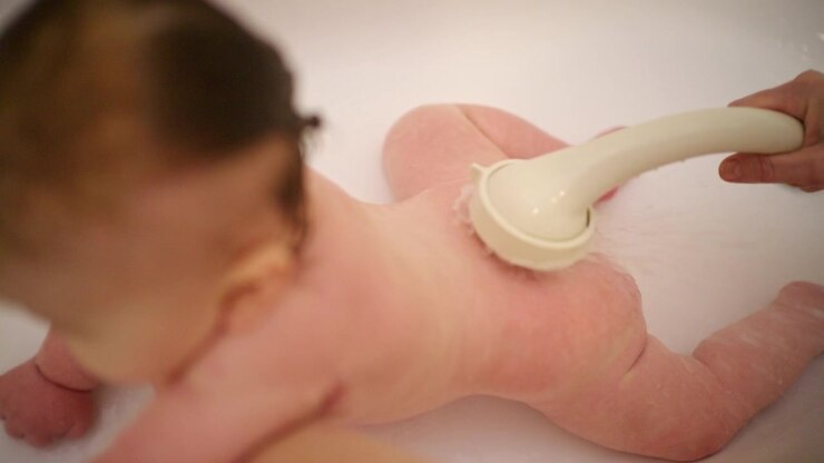 Set bagfra af en baby i badekarret, mens en voksen støtter babyens bryst og nakke nedefra, og babyen vender væk.