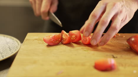 El-Chef-Corta-Cuidadosamente-Un-Tomate-Con-Un-Cuchillo-Sobre-Una-Tabla-De-Madera-Con-Las-Manos-Limpias,-Demostrando-Precisión-E-Higiene.