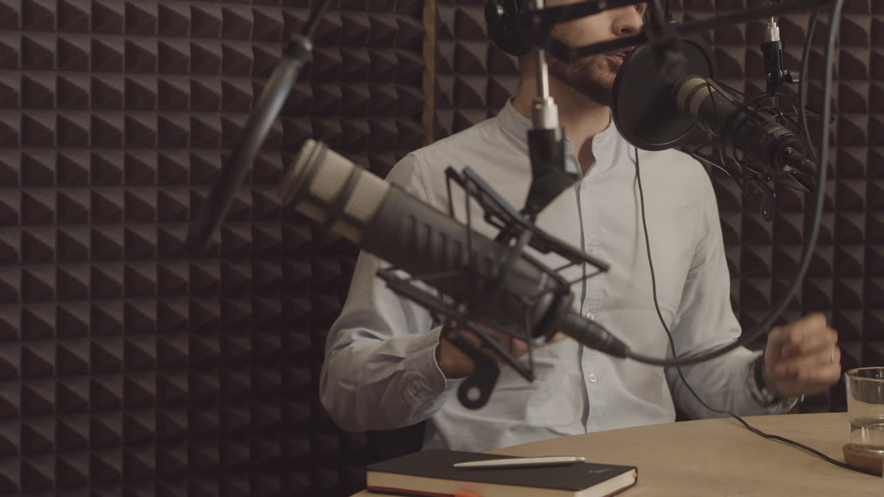 un joven expresivo habla de un tema interesante en un estudio de grabación de radio. en primer plano hay un micrófono desenfocado.