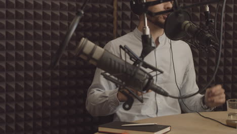 Expressive-young-man-man-talks-about-an-interesting-subject-in-a-radio-recording-studio.-In-the-foreground-there-is-a-microphone-out-of-focus.