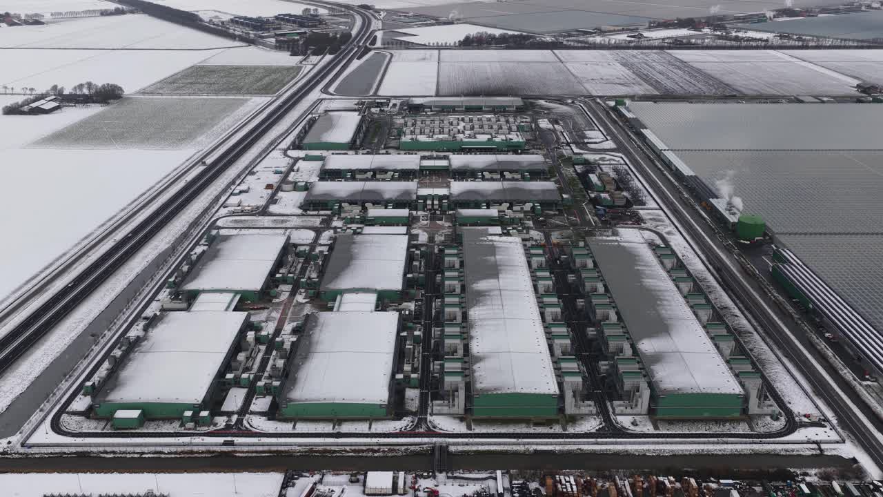 Aerial drone footage of a large hyperscale computing center in wintertime, showing industrial scale data center infrastructure powering cloud computing, artificial intelligence, and global digital ser