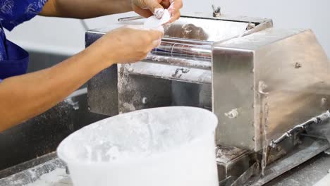 person rolling dough through a machine in a bakery