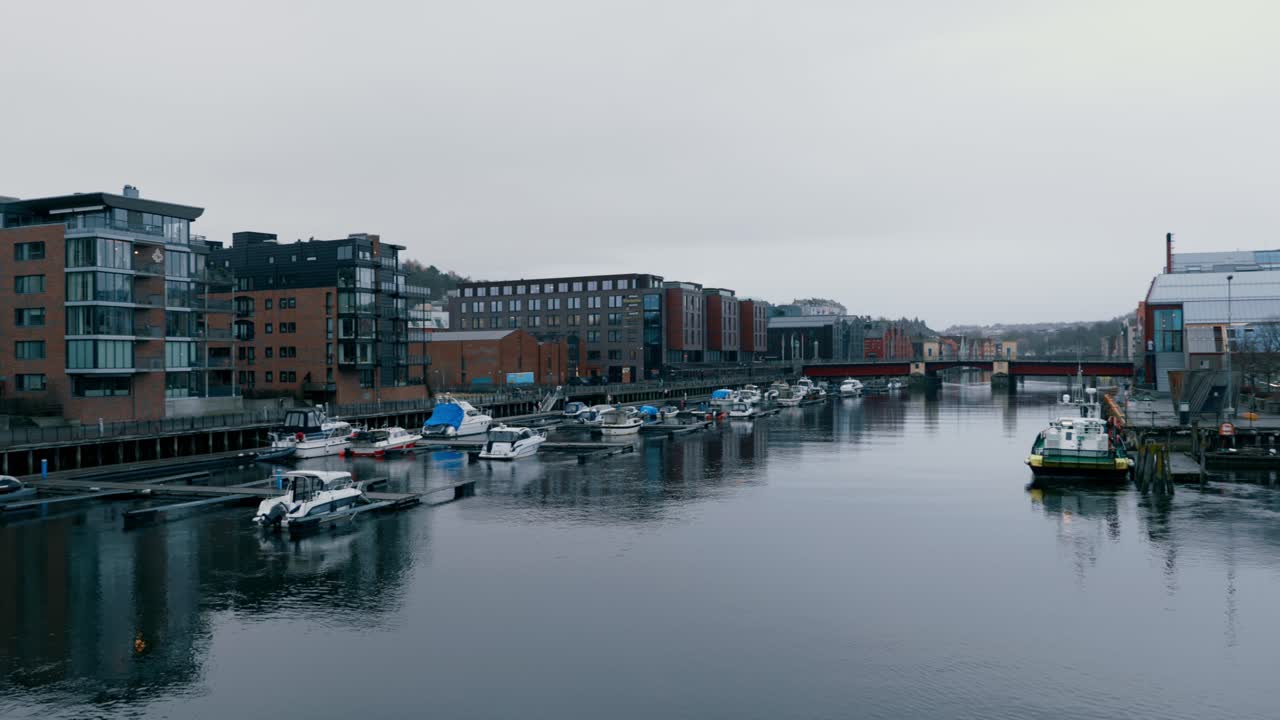 Panning across the Solsiden marina of Trondheim, Norway. Boats docked surrounded by residential and industrial modern buildings. Cold misty morning.