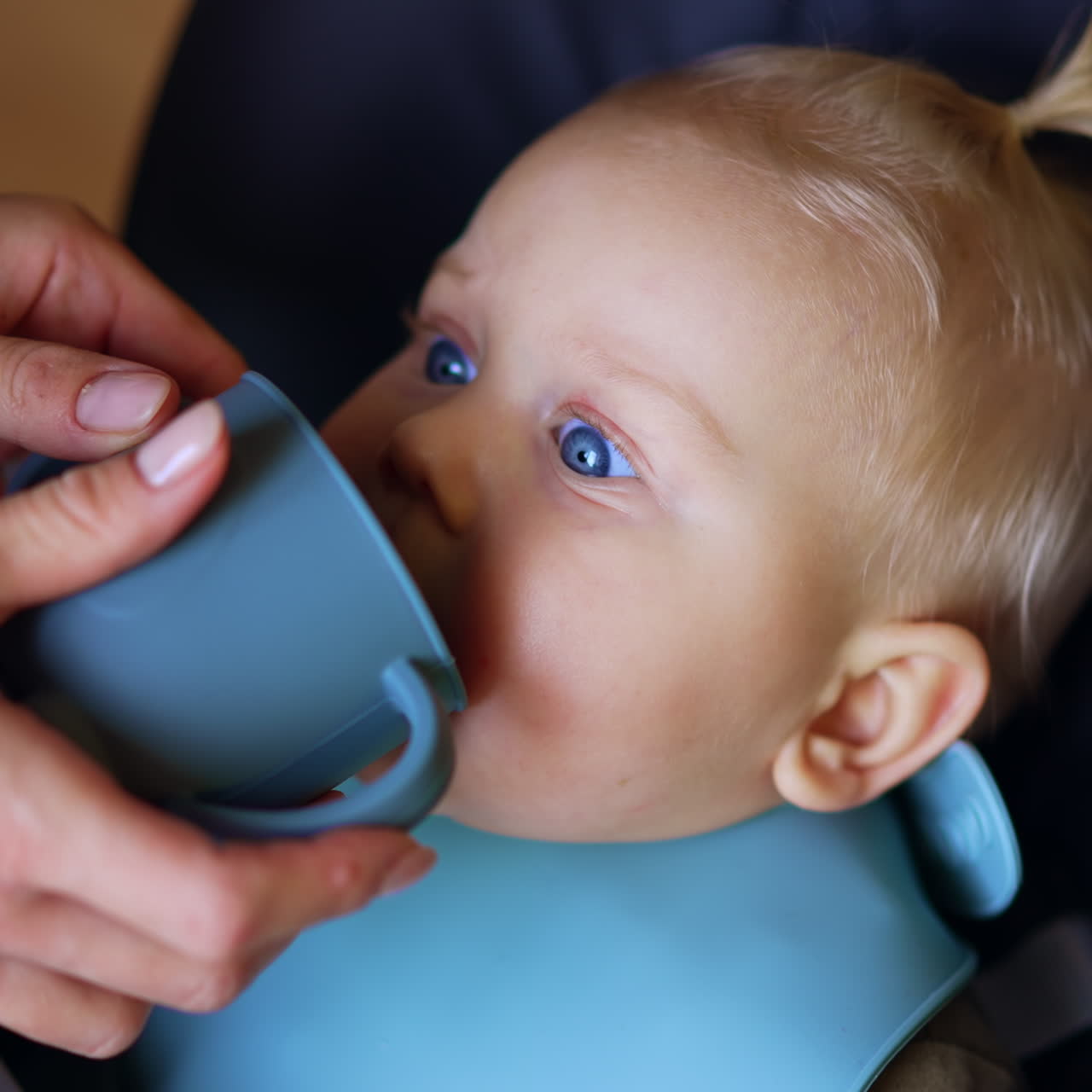 A un tenero neonato caucasico viene data una tazza da cui bere. Primo piano. La madre sta nutrendo il suo bambino.