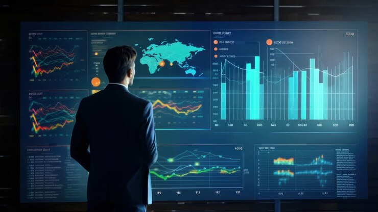 A man in a suit analyzes digital graphs on a large screen. The video captures a rear angle