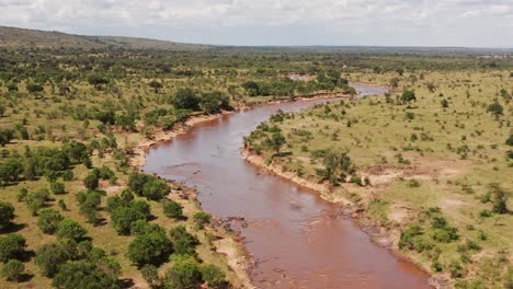 Aerial-drone-shot-of-Masai-Mara-River-Landscape-Winding-in-Beautiful-Scenery-in-Maasai-Mara-National-Reserve-in-Kenya,-Africa,-Wide-Establishing-Shot-with-Greenery-and-Lush-Green-Trees