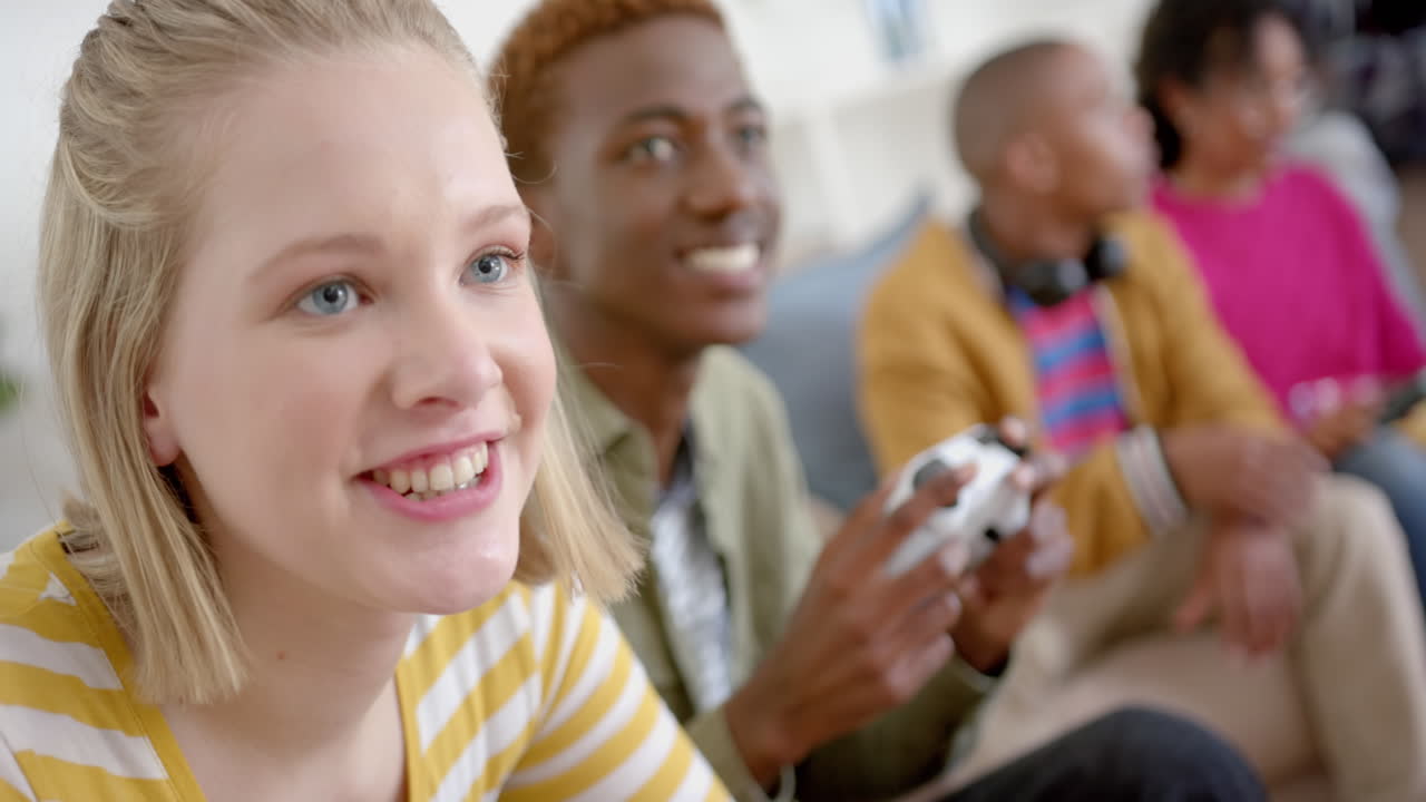 Happy diverse group of teenage friends sitting on couch and playing video games at home, slow motion