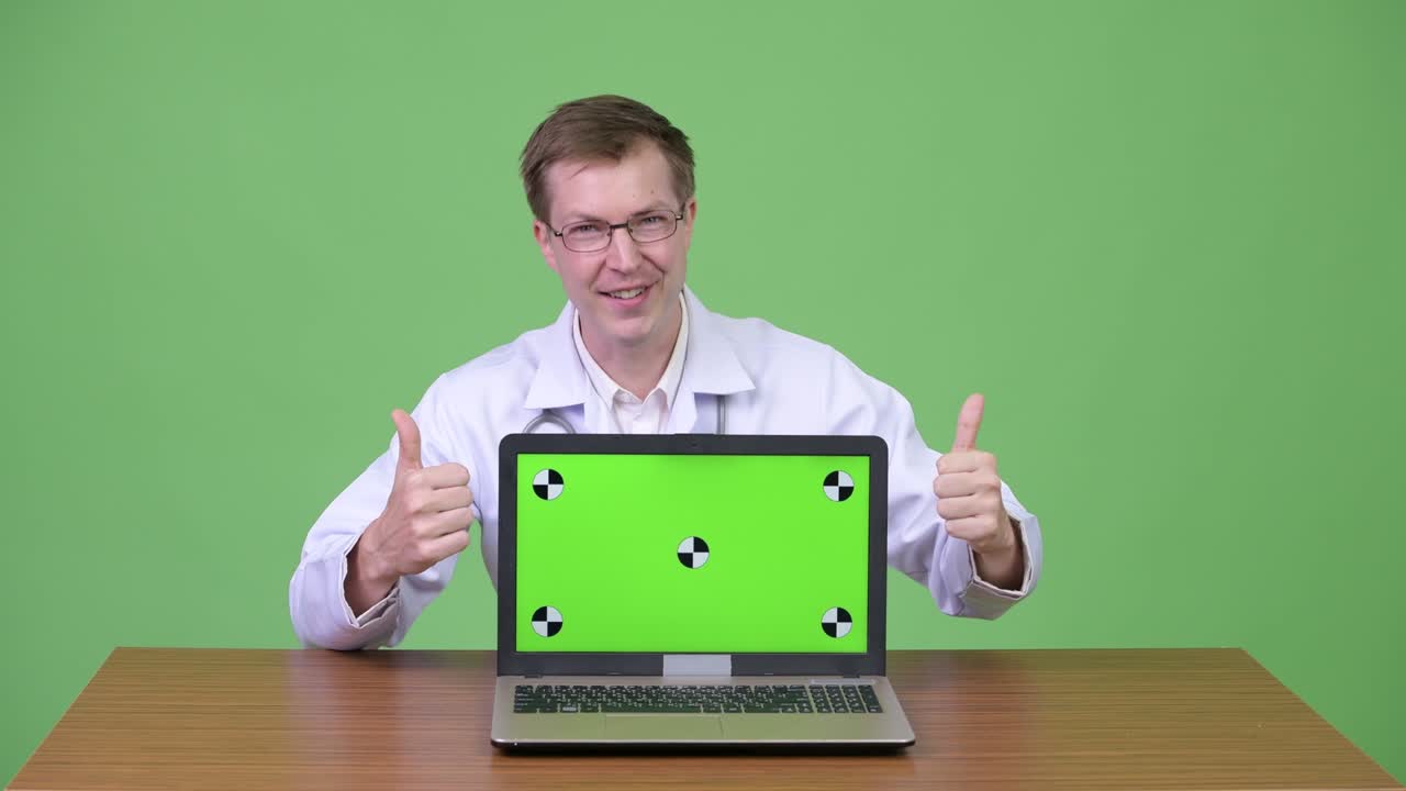 médico sentado y mostrando pantalla verde computadora portátil mientras habla