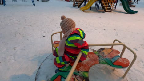 cheerful kid on playground spinner in winter