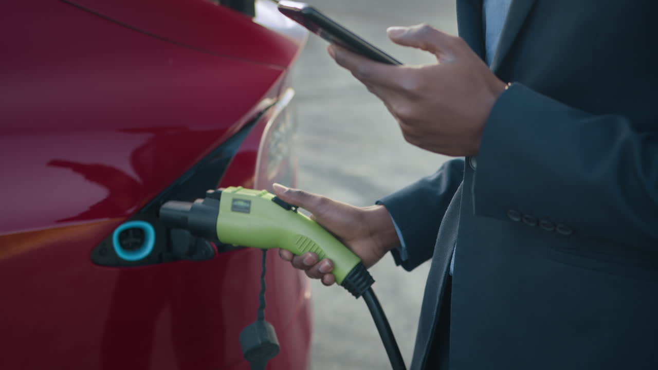 전기 자동차를 충전하고 스마트폰을 사용하는 사업가