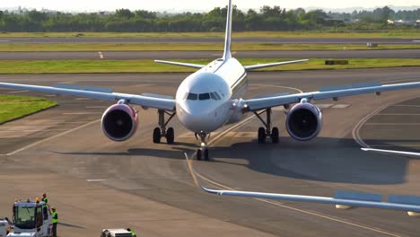 two airplanes taxi on a busy airfield as ground crew members guide them. the scene captures the vibrant colors of sunset on the horizon, enhancing the airport's bustling atmosphere.