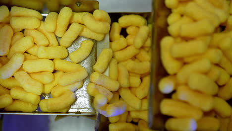 delicious crispy corn sticks on the conveyor belt. metal boxes being filled with yellow snacks at automated line at food factory.