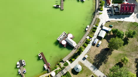 op-down aerial view of a marina and boats docked on the green waters of a lake in ryn, warmia-masuria