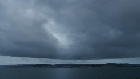 dark storm clouds over water and distant city