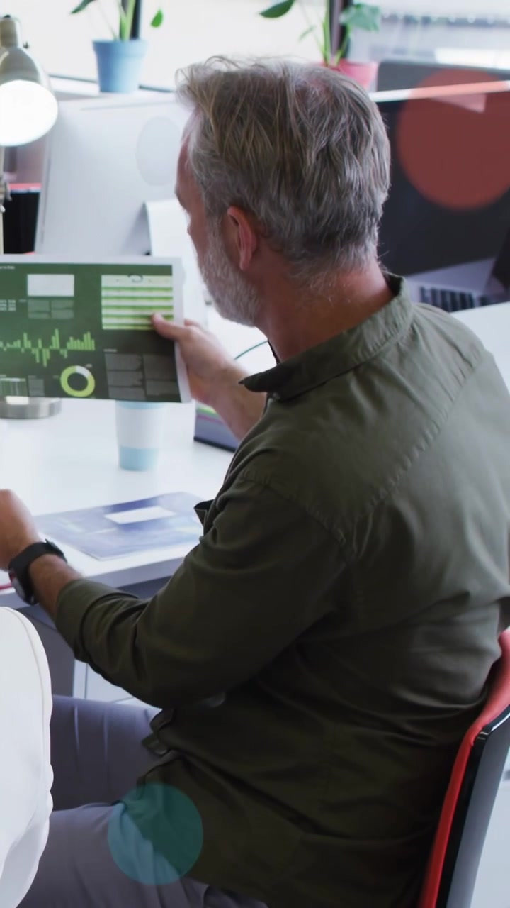 Vertical video: Man tilting report, reading business charts while shapes passing, talking with peer