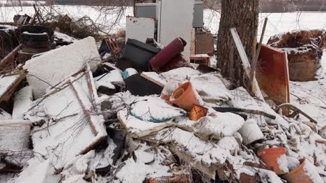 pile of household garbage in countryside yard near bare tree, winter environment