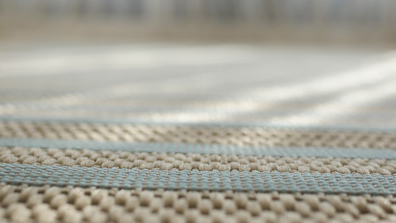 Close-up view of a woven rug with beige and teal stripes