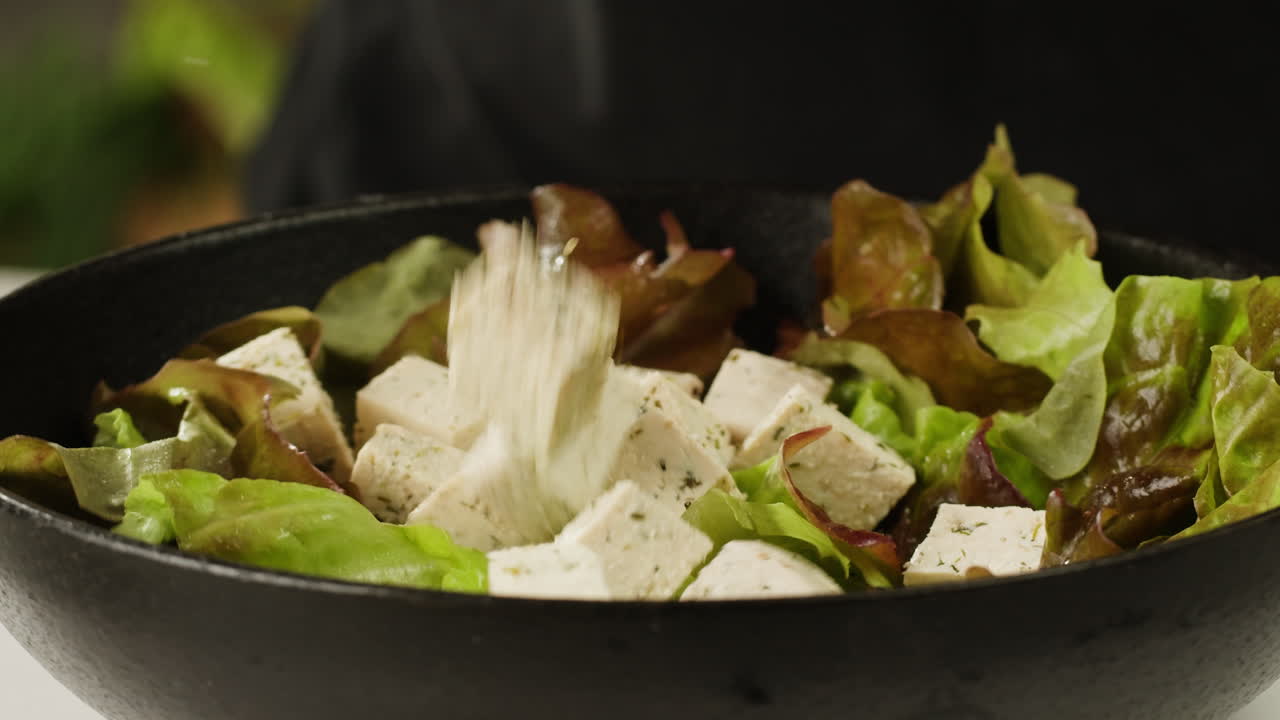 Fried tofu with sesame seeds and spices on cast iron pan, cooking japanese salad. Healthy ingredient for cooking vegan vegetarian diet food. Roasted tofu over black background.