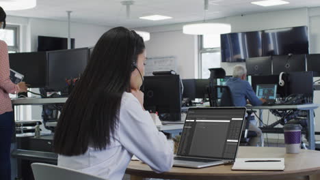 asian woman sitting at desk watching coding data processing on laptop screen