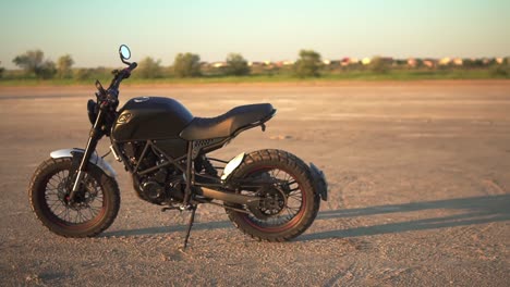 A-black-motorcycle-parking-on-the-ground-outdoors,-green-strip-of-trees-on-blurred-background