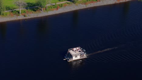 Drone-aerial-view-of-party-barge-with-people-sunbathing-moving-on-a-slow-river-in-summer-sun