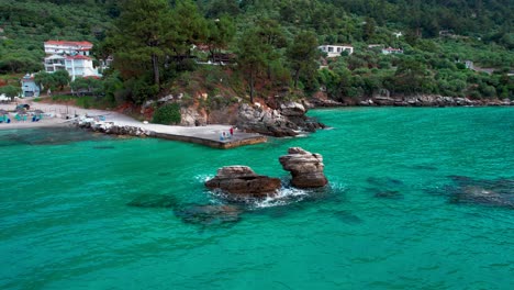 rotating aerial view with a small cliff in the foreground and the famous golden beach in the background with towering mountain peaks, thassos island, greece