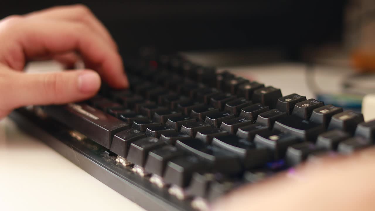 primer plano de las manos de un hombre interactuando con un teclado rgb en un escritorio de computadora sucio con una pequeña profundidad de campo