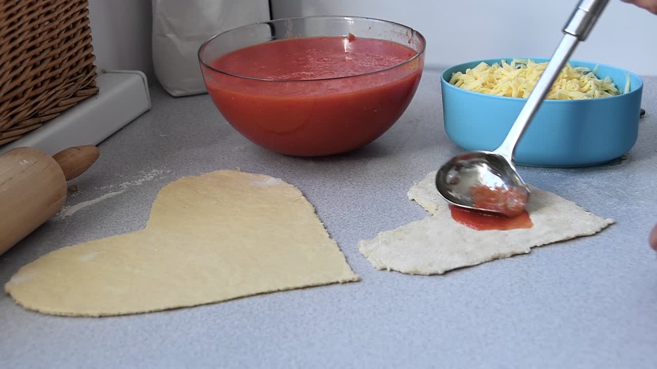 작은 하트 모양의 피자 반죽에 토마토 소스를 얹은 남성 손 클로즈업