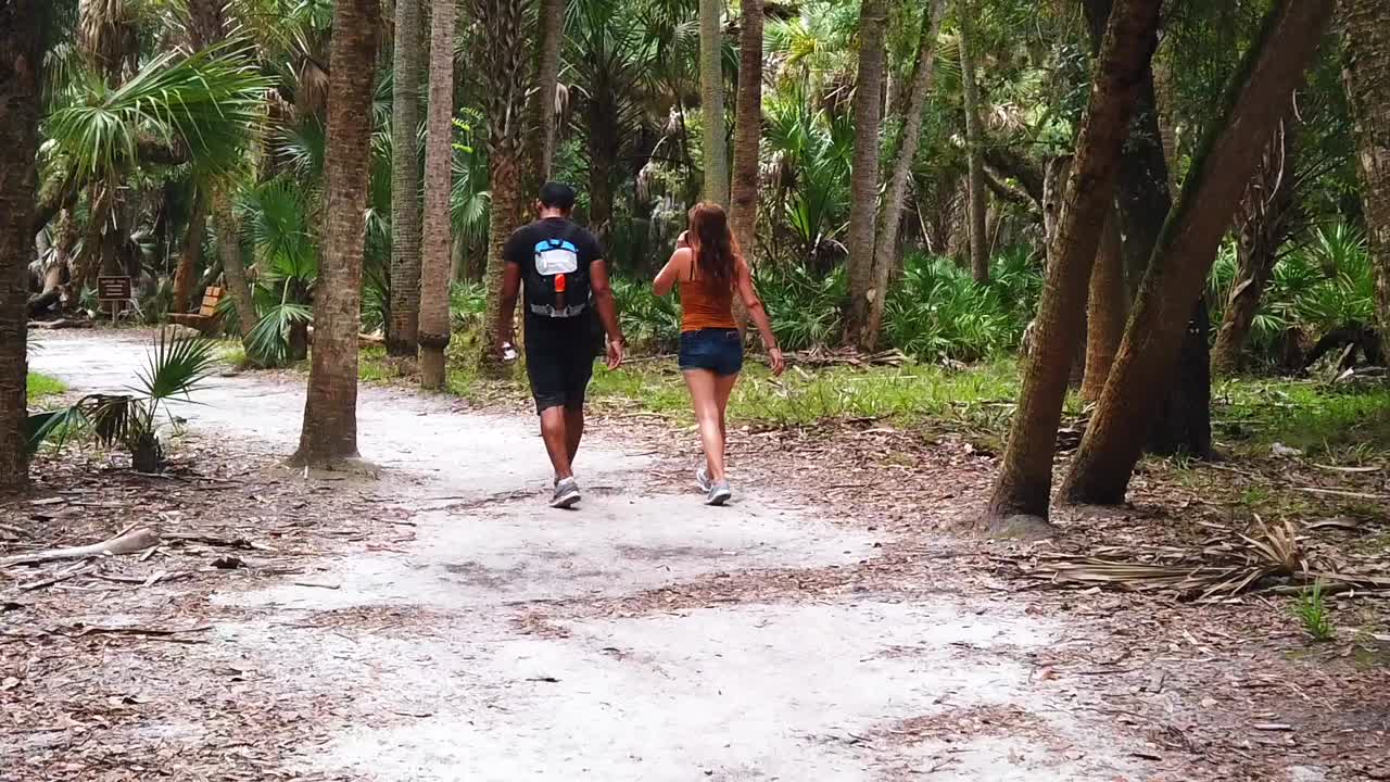 attractive man and woman couple walking through the palm trees during a romantic summer holiday, spending quality time, slow motion gimbal shot in Florida