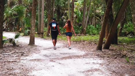 Atractiva-Pareja-De-Hombre-Y-Mujer-Caminando-A-Través-De-Las-Palmeras-Durante-Unas-Vacaciones-Románticas-De-Verano,-Pasando-Tiempo-De-Calidad,-Tiro-De-Cardán-En-Cámara-Lenta-En-Florida